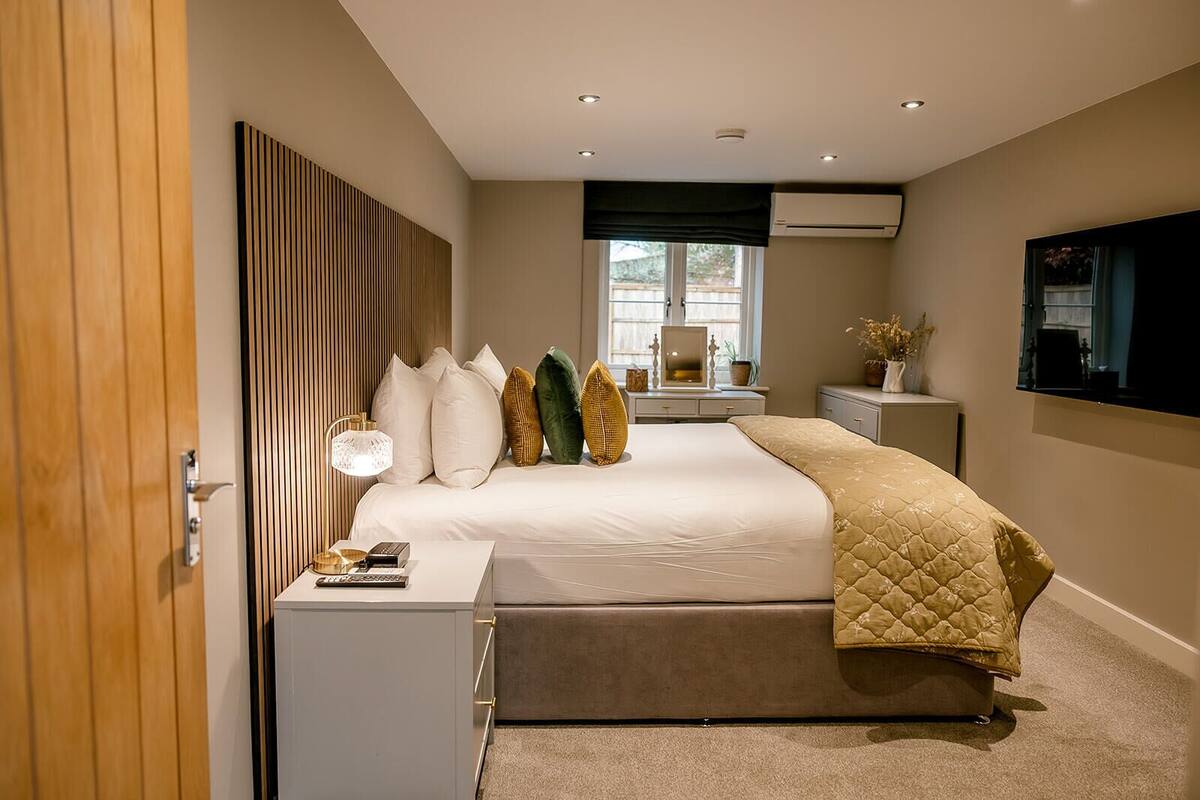 A modern bedroom with a bed, bedside tables, a lamp, a mirror, and a TV.