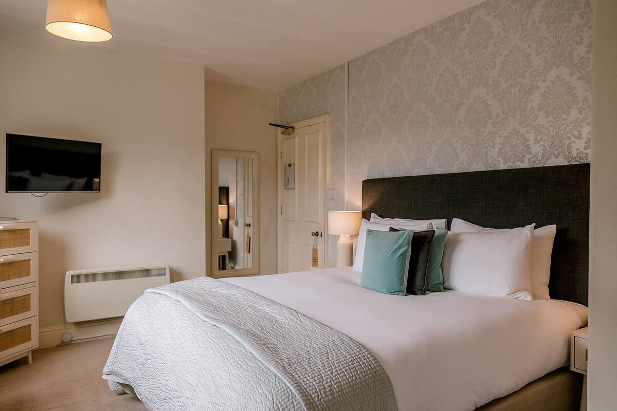 A neatly arranged hotel room with a large bed, a television mounted on the wall, a dresser, and a mirror.