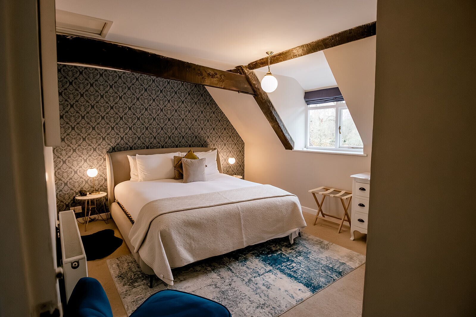 Une chambre à coucher comprenant un lit, des tables de chevet, une commode, une fenêtre et un mur décoré d’un motif.
