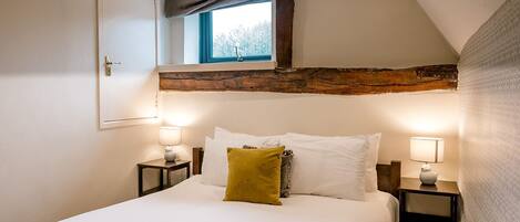A bedroom with a large bed, two bedside tables with lamps, a window with a view, and exposed wooden beams.