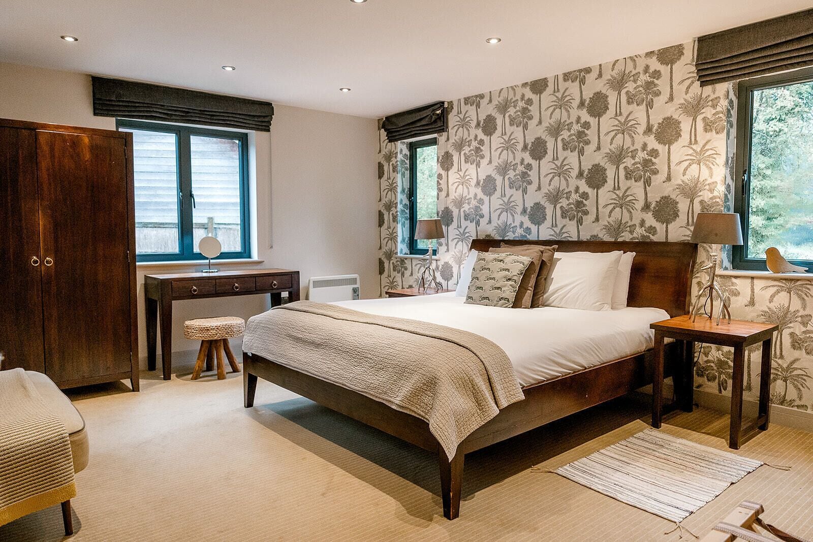 A bedroom with a large bed, a wooden wardrobe, a desk, and a window with a view of trees.