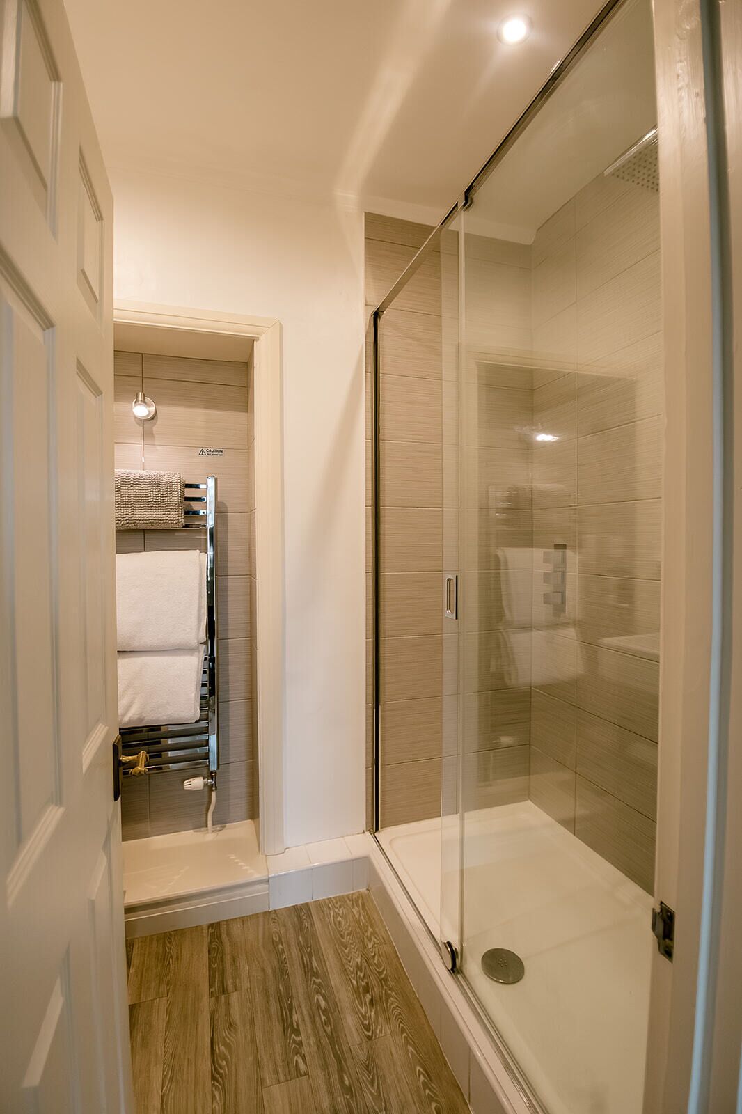 A modern bathroom with a glass shower enclosure, a wooden floor, and a towel rack with towels.