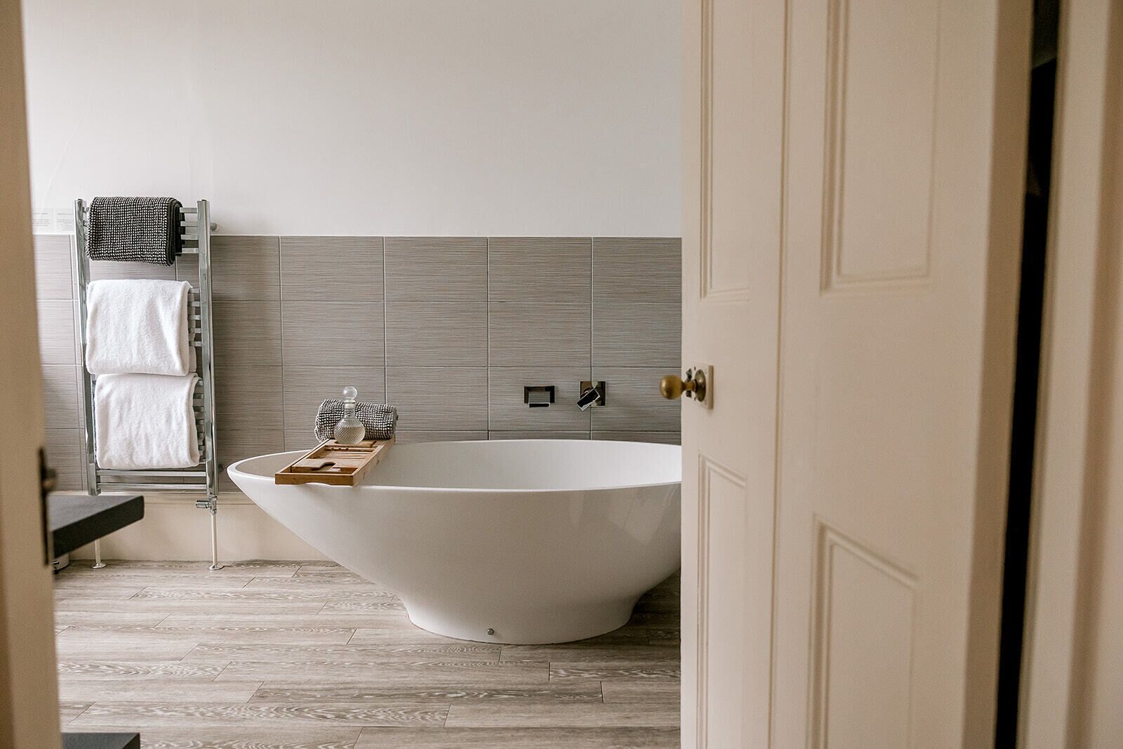 A modern bathroom with a freestanding bathtub, a towel rack with towels, and a wooden tray with toiletries.