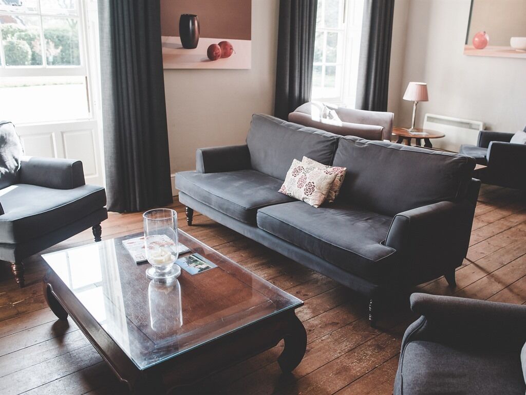 A modern living room with a grey sofa, a glass coffee table, and a wooden floor.