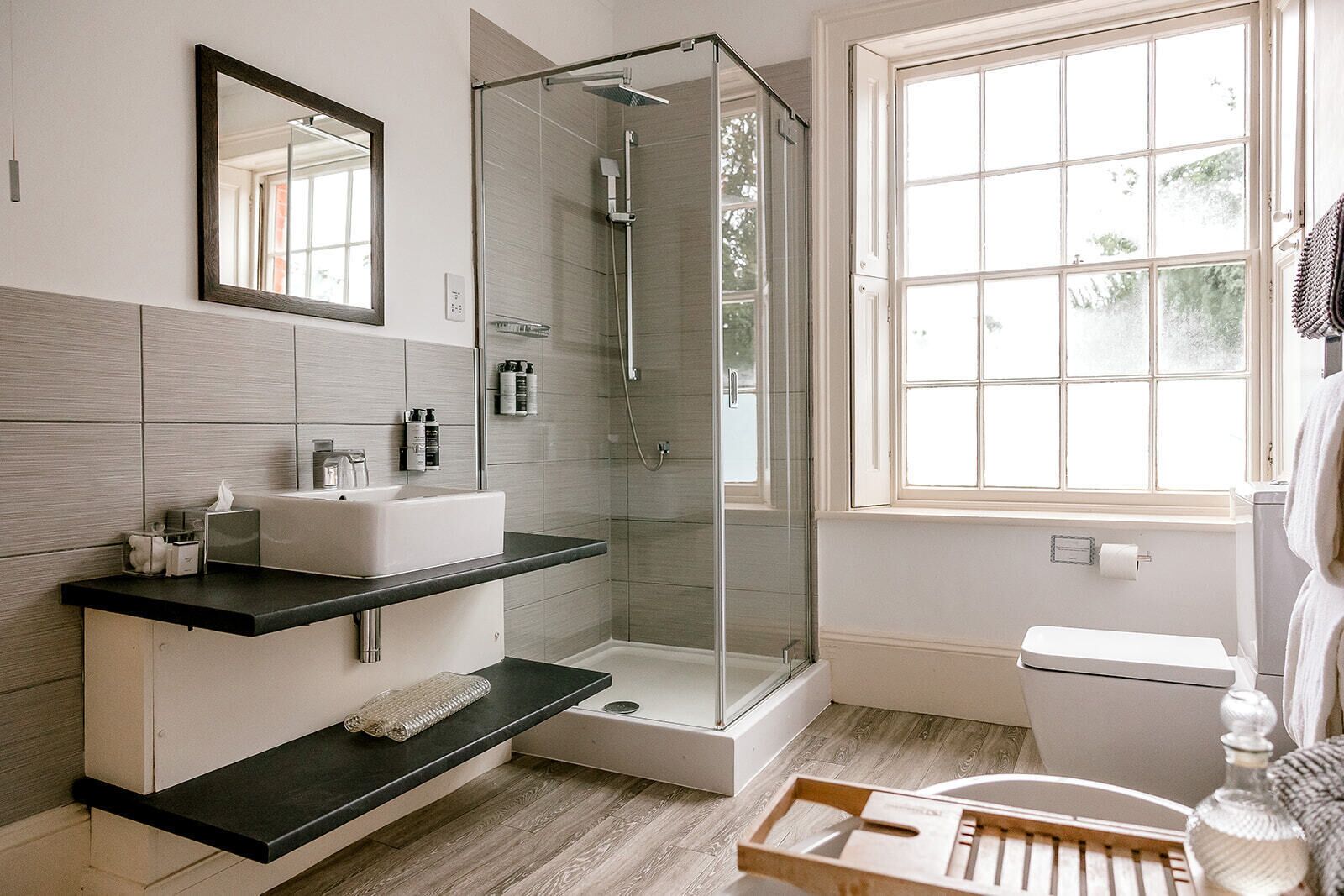 A modern bathroom with a glass-enclosed shower, a white sink, and a large window providing natural light.