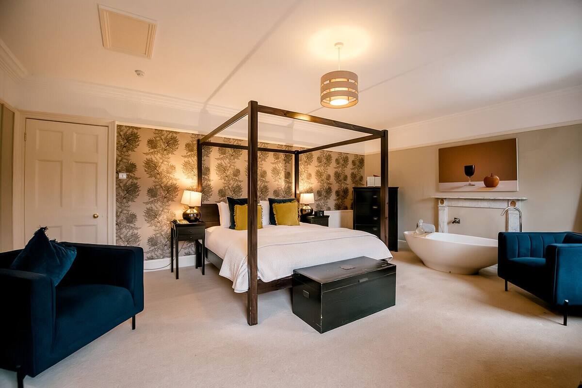 A four-poster bed with a canopy, a large bathtub, and two armchairs.
