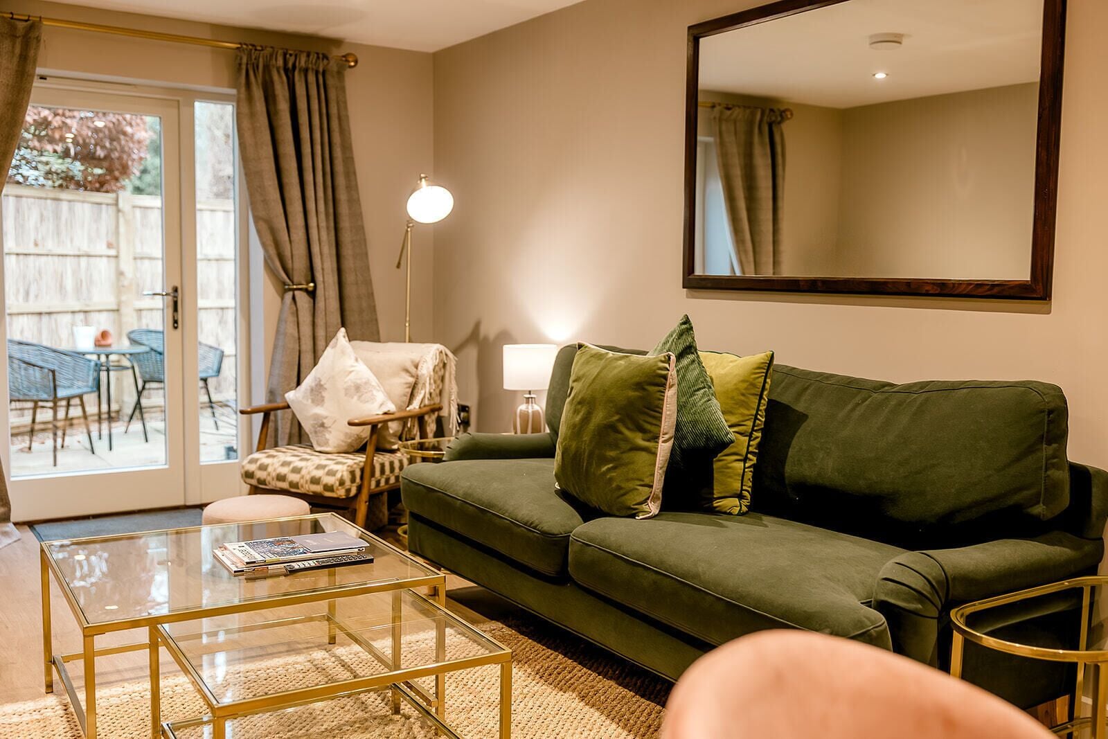 A living room with a green sofa, a glass coffee table, a chair, and a large mirror on the wall.