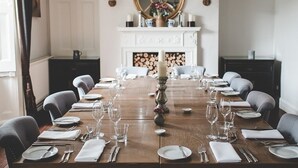 Une salle à manger avec une longue table en bois dressée pour le repas, une cheminée et un miroir au mur.