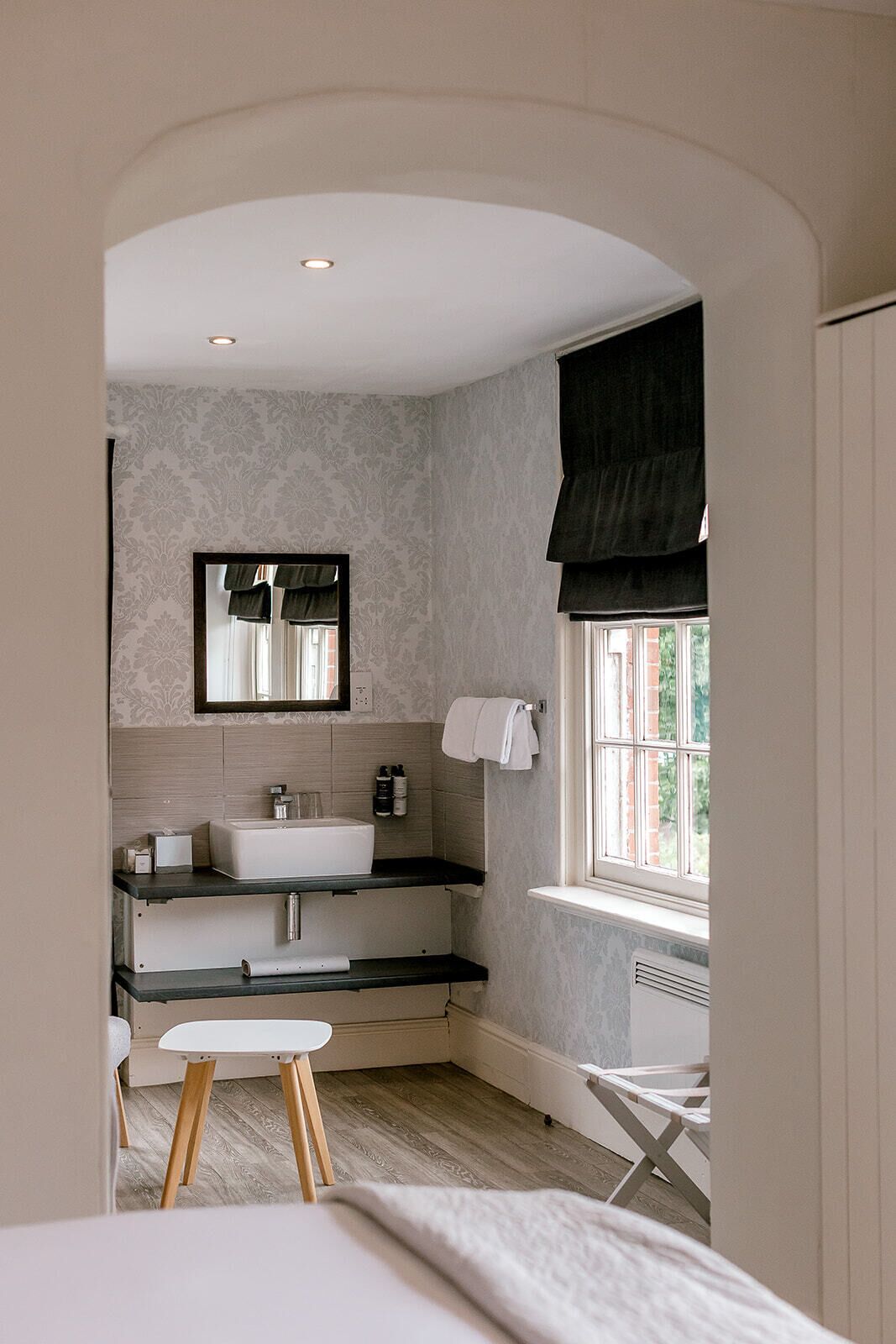 Une salle de bain moderne avec un lavabo sur pied, un miroir et une fenêtre donnant sur un paysage verdoyant.
