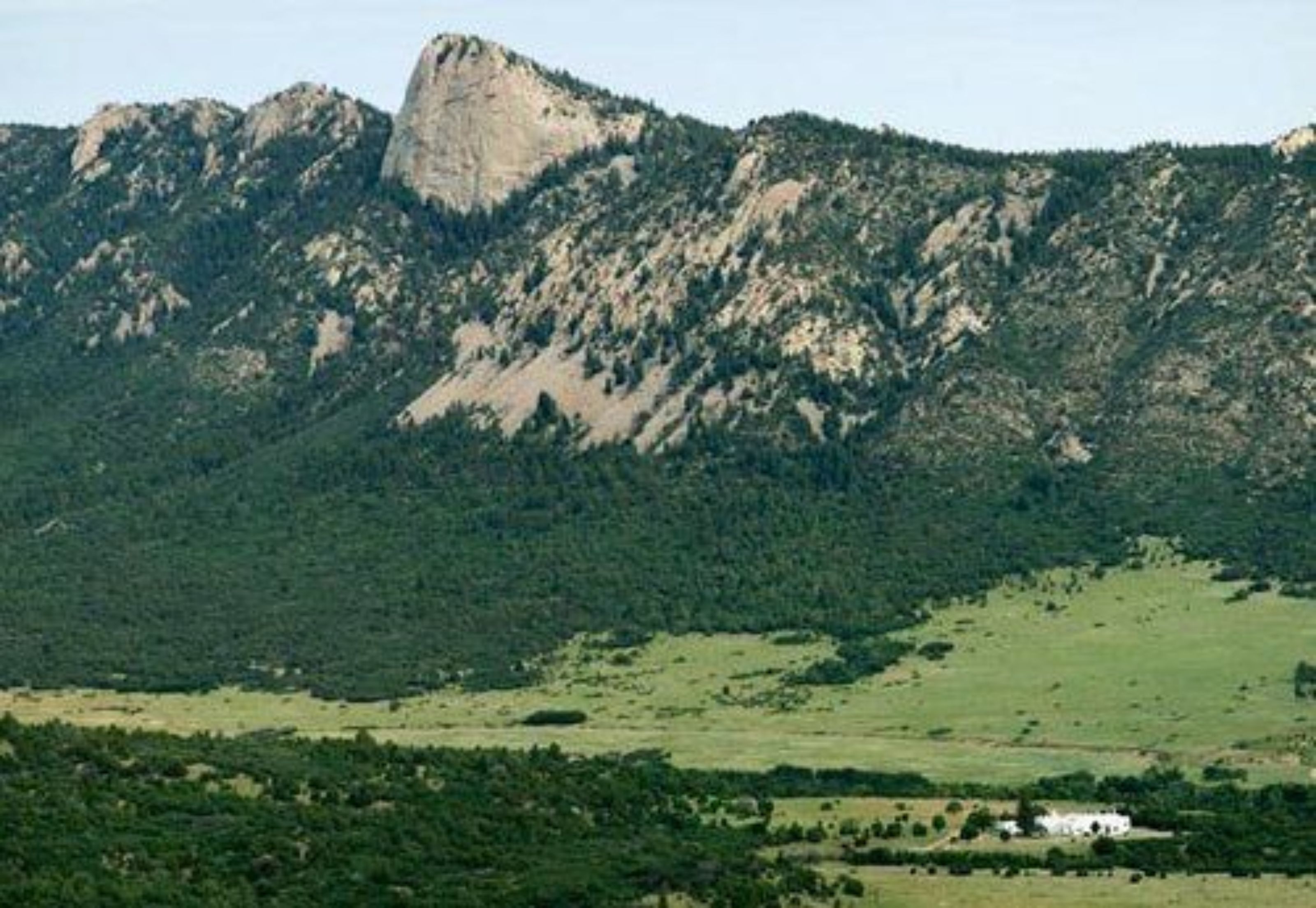 Un paisaje montañoso con un pico rocoso destacado y un edificio blanco al frente.