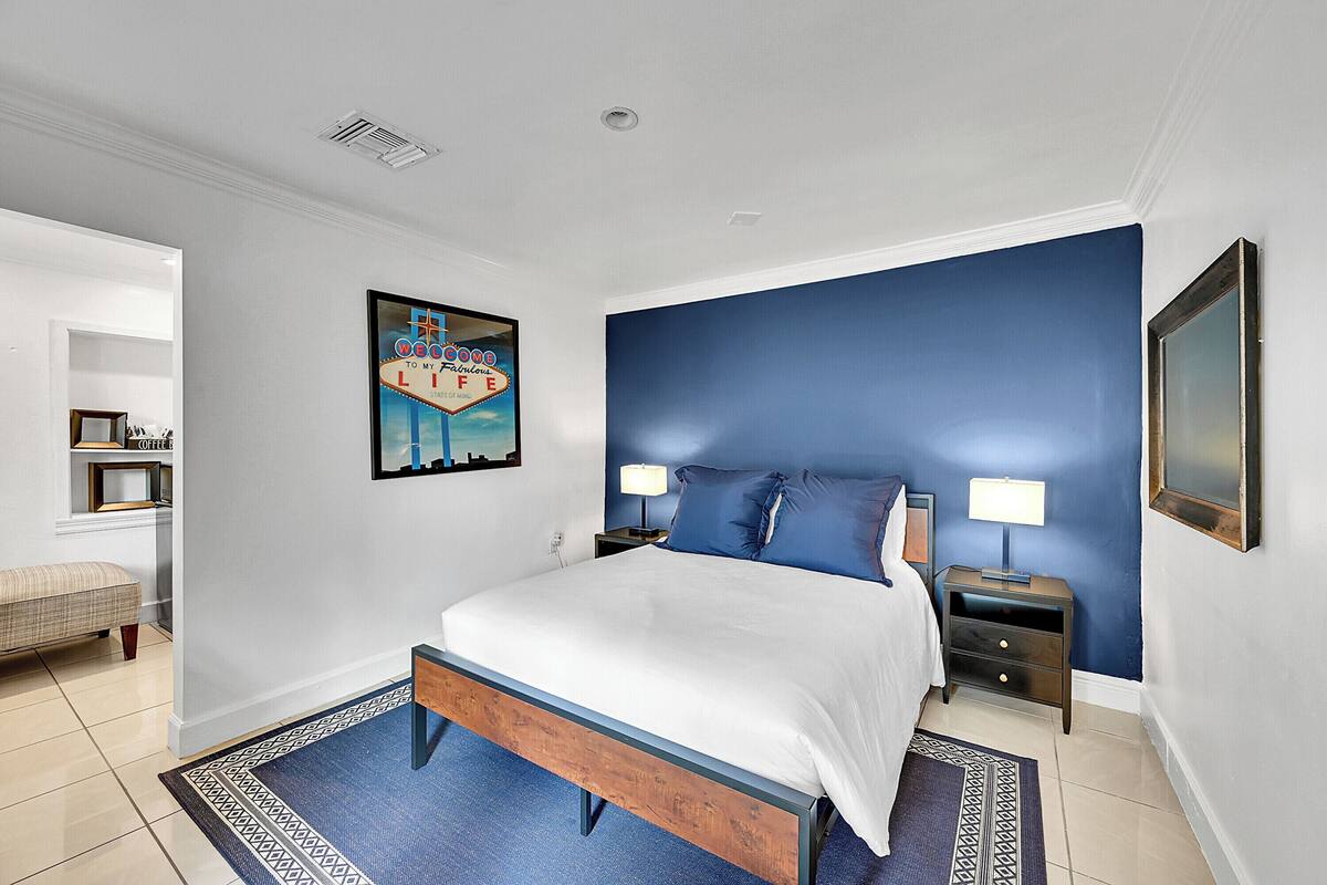 A bedroom with a bed, two bedside tables, a nightstand, a blue accent wall, a framed picture, and a patterned rug.
