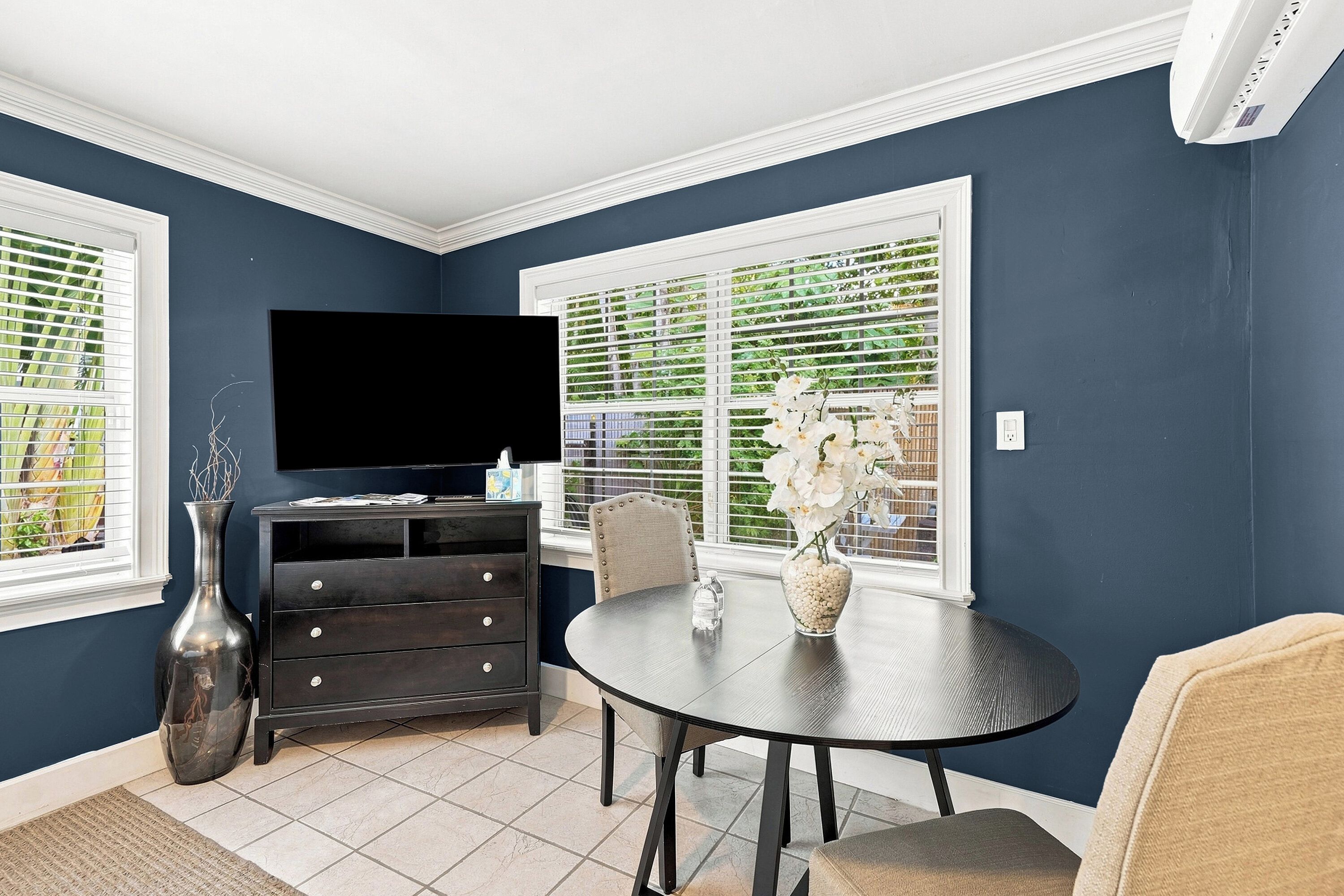 A dining area with a round table, chairs, a television, and a vase with flowers.