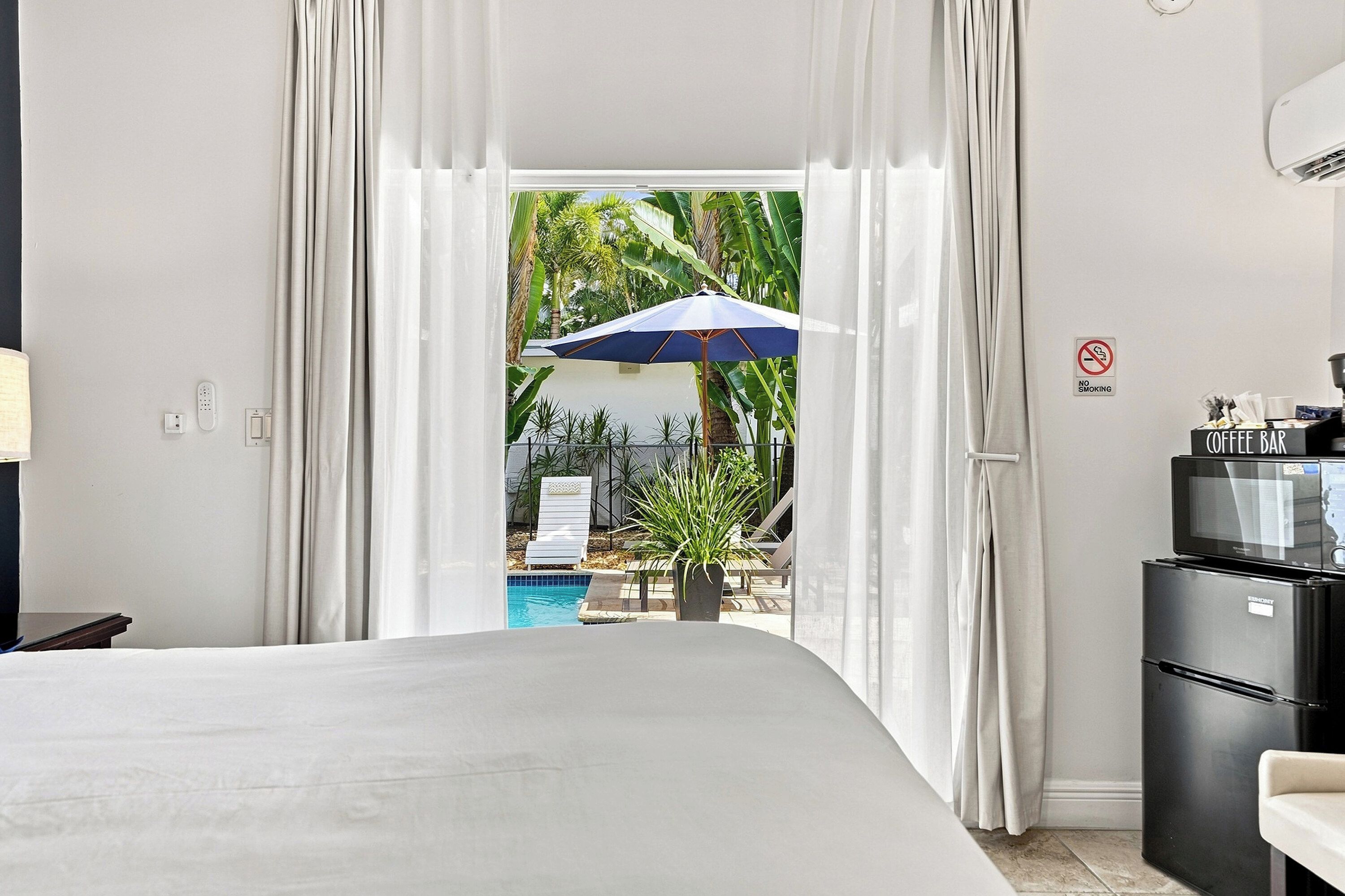 Habitación de hotel con cama, una barra de café, televisión y vista a una piscina y palmeras.