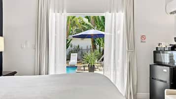 A hotel room with a bed, a coffee bar, a TV, and a view of a pool and palm trees.
