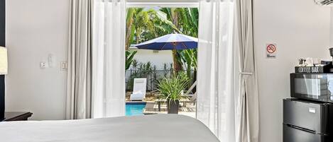 Habitación de hotel con cama, una barra de café, televisión y vista a una piscina y palmeras.