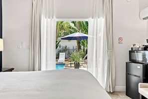A hotel room with a bed, a coffee bar, a TV, and a view of a pool and palm trees. - Inn On The Drive (Adults Only) (Wilton Manors)