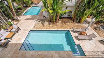 Una piscina rectangular con borde de azulejos, rodeada de sillas de descanso y palmeras.