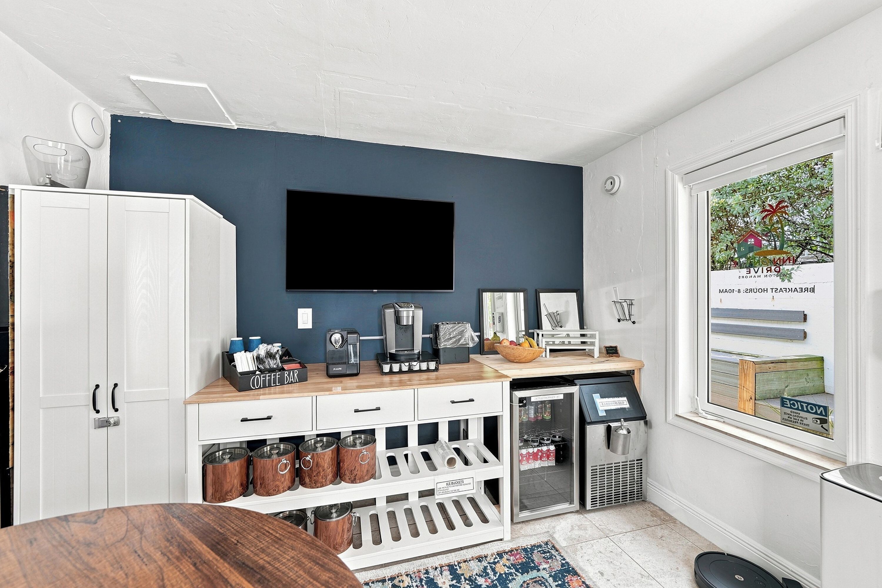 A modern kitchen with a coffee bar, a refrigerator, and a large window with a view of a beach.