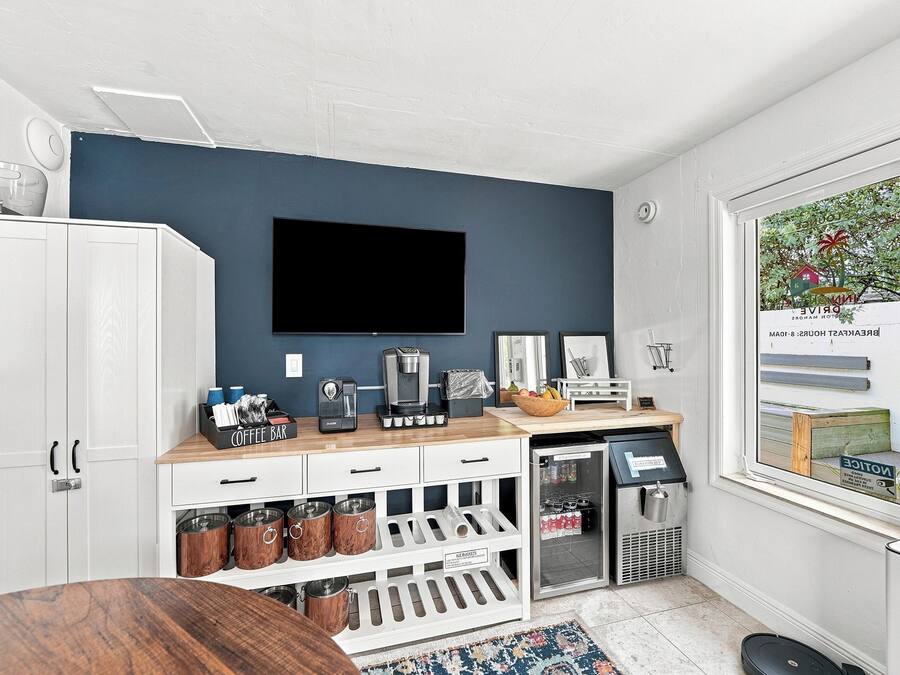 A modern kitchen with a coffee bar, a refrigerator, and a large window with a view of a beach.