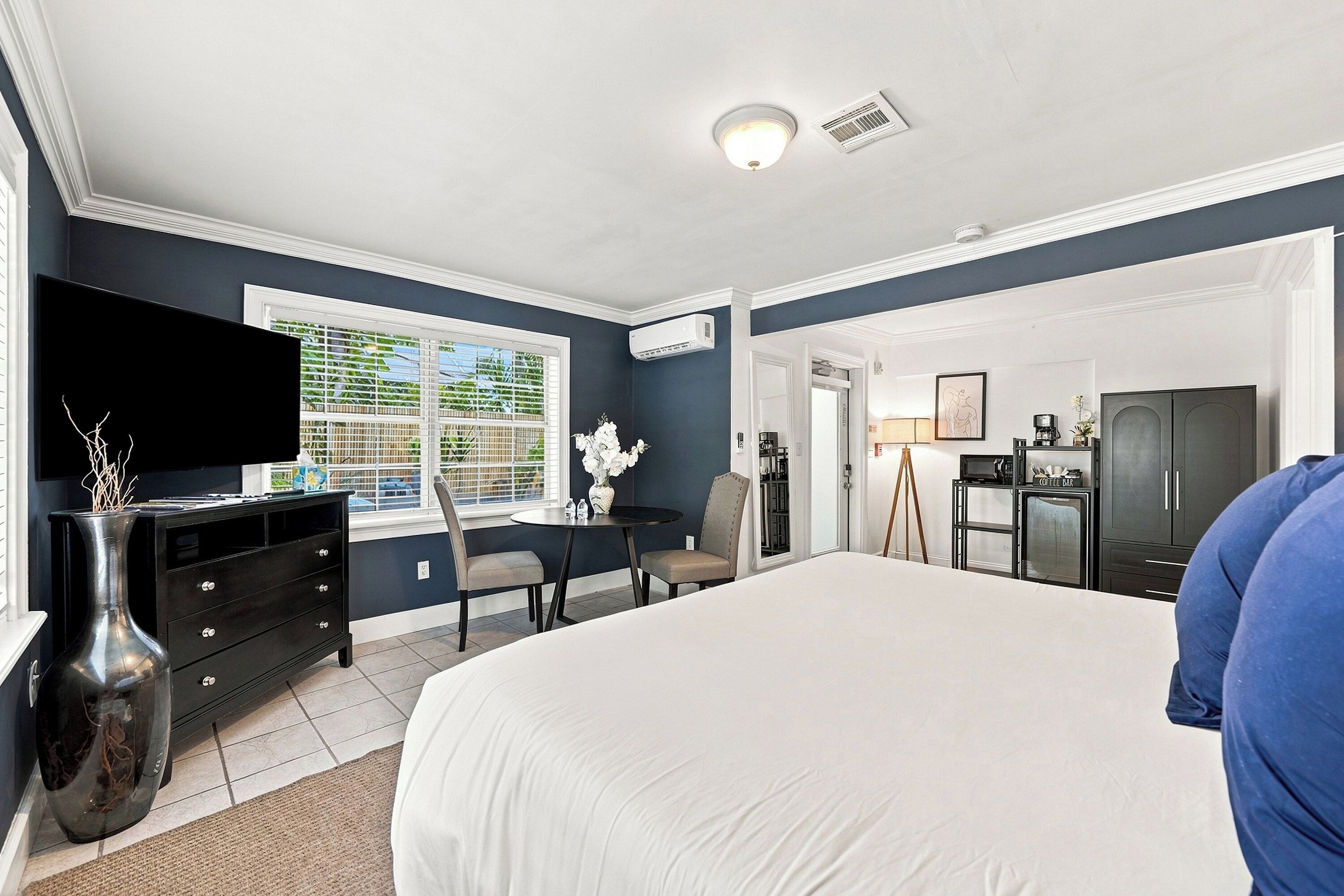 A hotel room with a bed, a desk, a chair, a television, and a window with blinds.