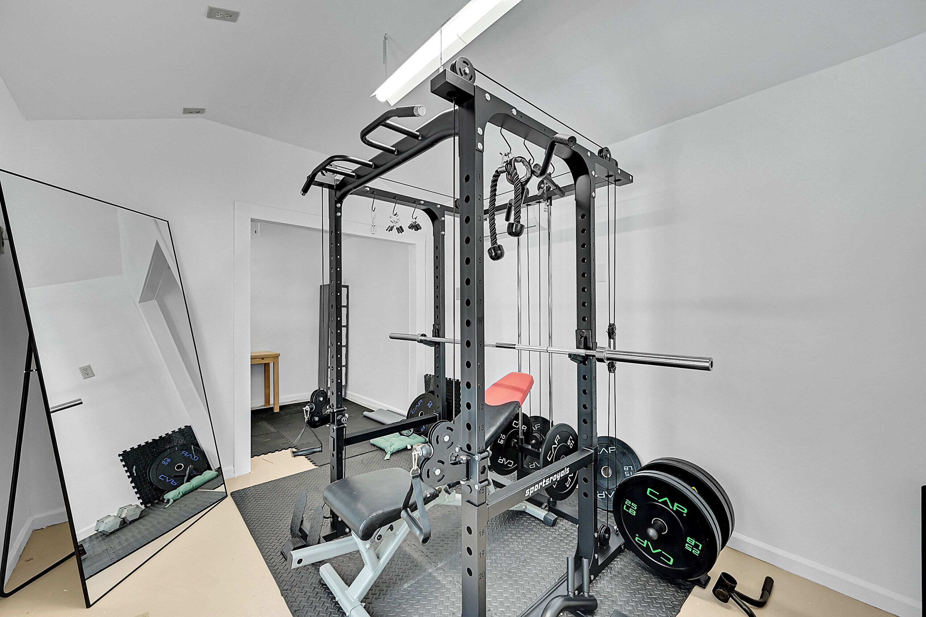 Un gimnasio en casa con una estructura para sentadillas, una prensa de banca y varios discos de pesas.