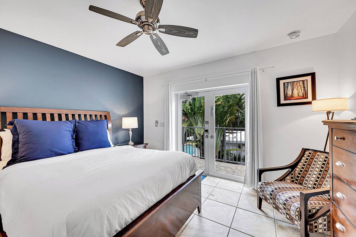 A bedroom with a bed, a ceiling fan, a chair, a dresser, and a sliding glass door leading to a balcony.