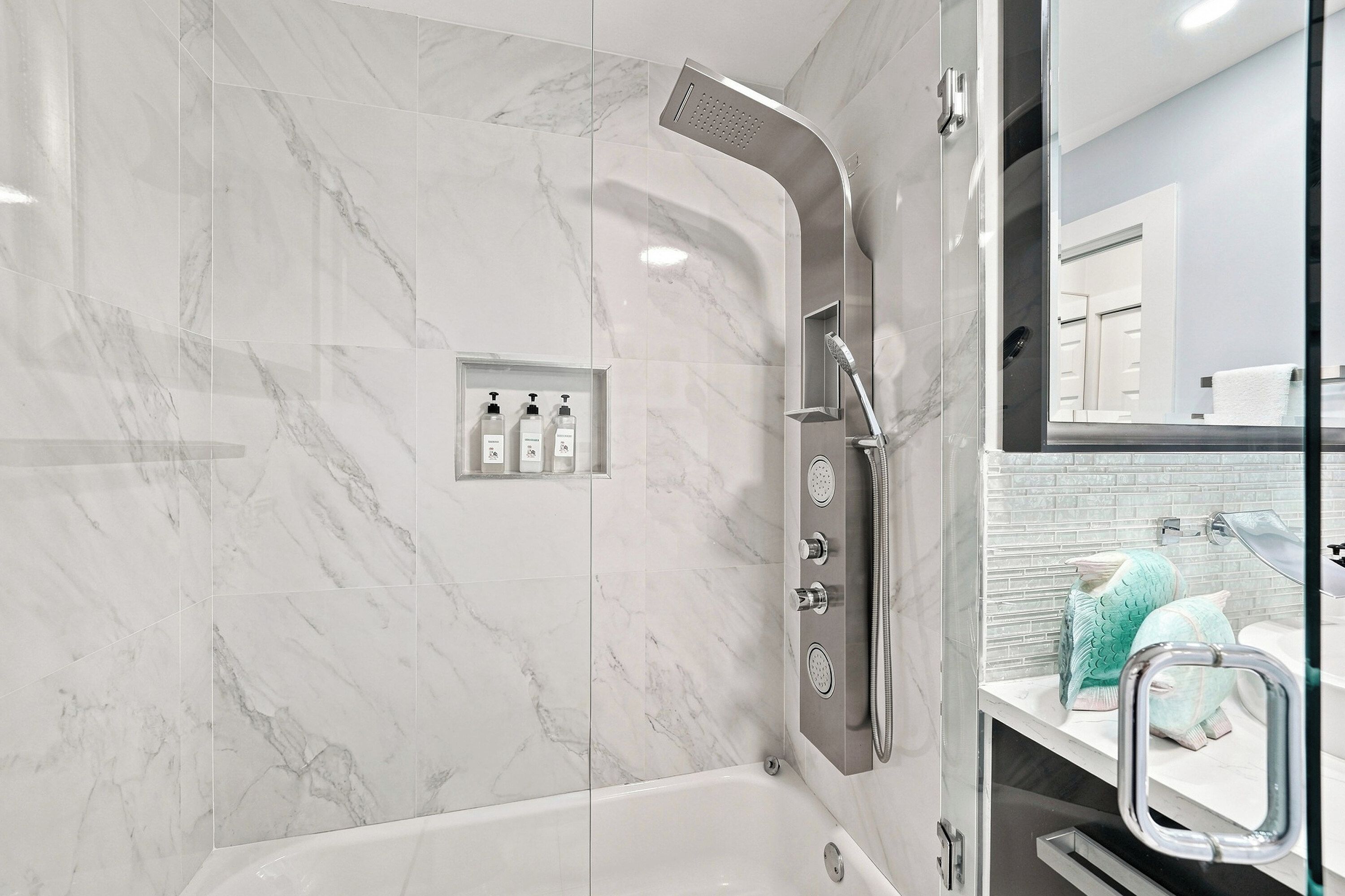 A modern bathroom with a glass-enclosed shower, a white marble wall, and a visible bathroom sink with a towel rack.