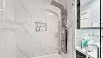 A modern bathroom with a glass-enclosed shower, a white marble wall, and a visible bathroom sink with a towel rack.