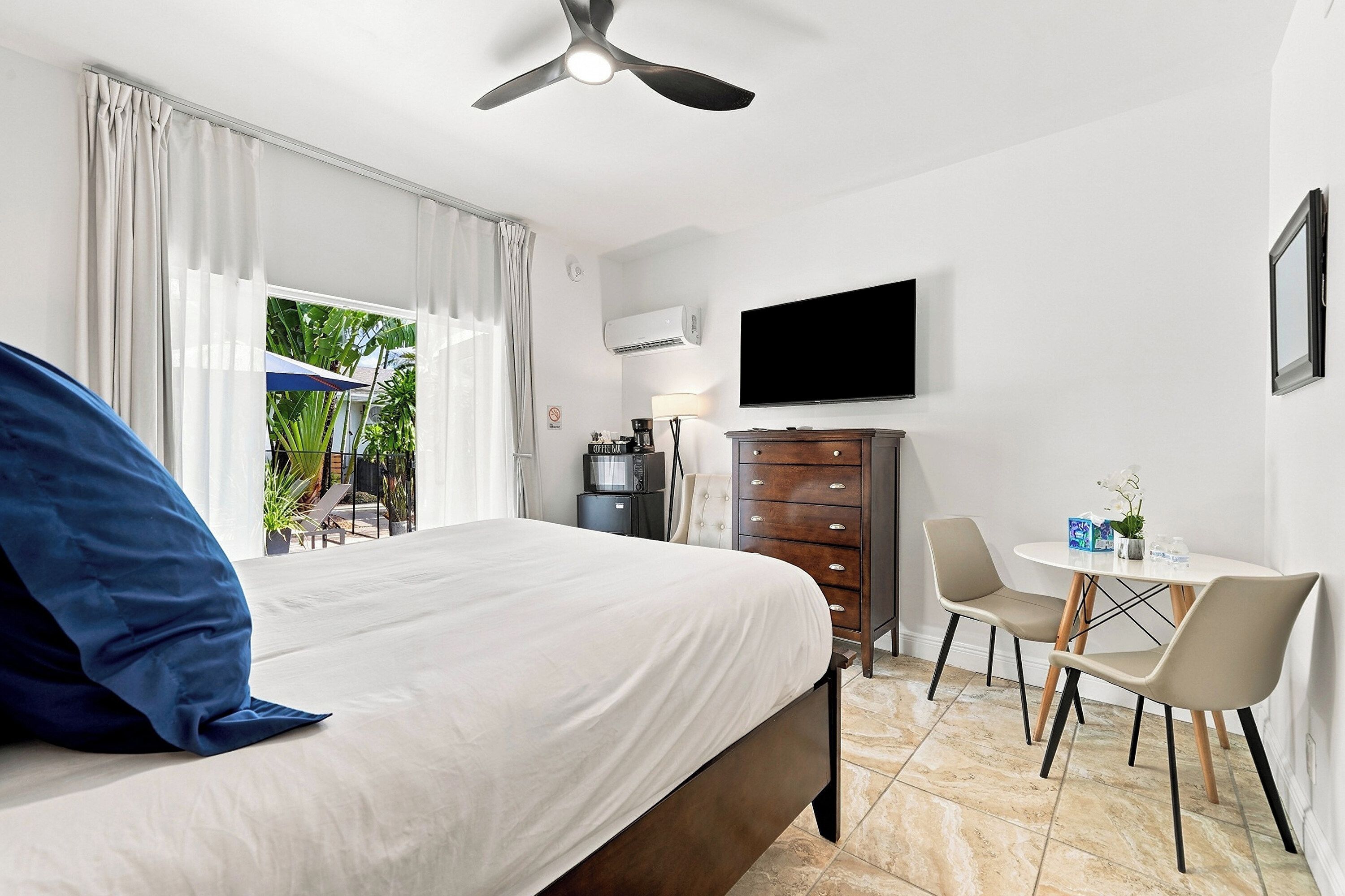 Een hotelkamer met een bed, een bureau, een stoel, een televisie en een plafondventilator.