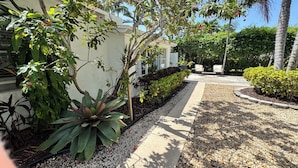 A landscaped outdoor area with a pathway, various plants, and a seating area with chairs.