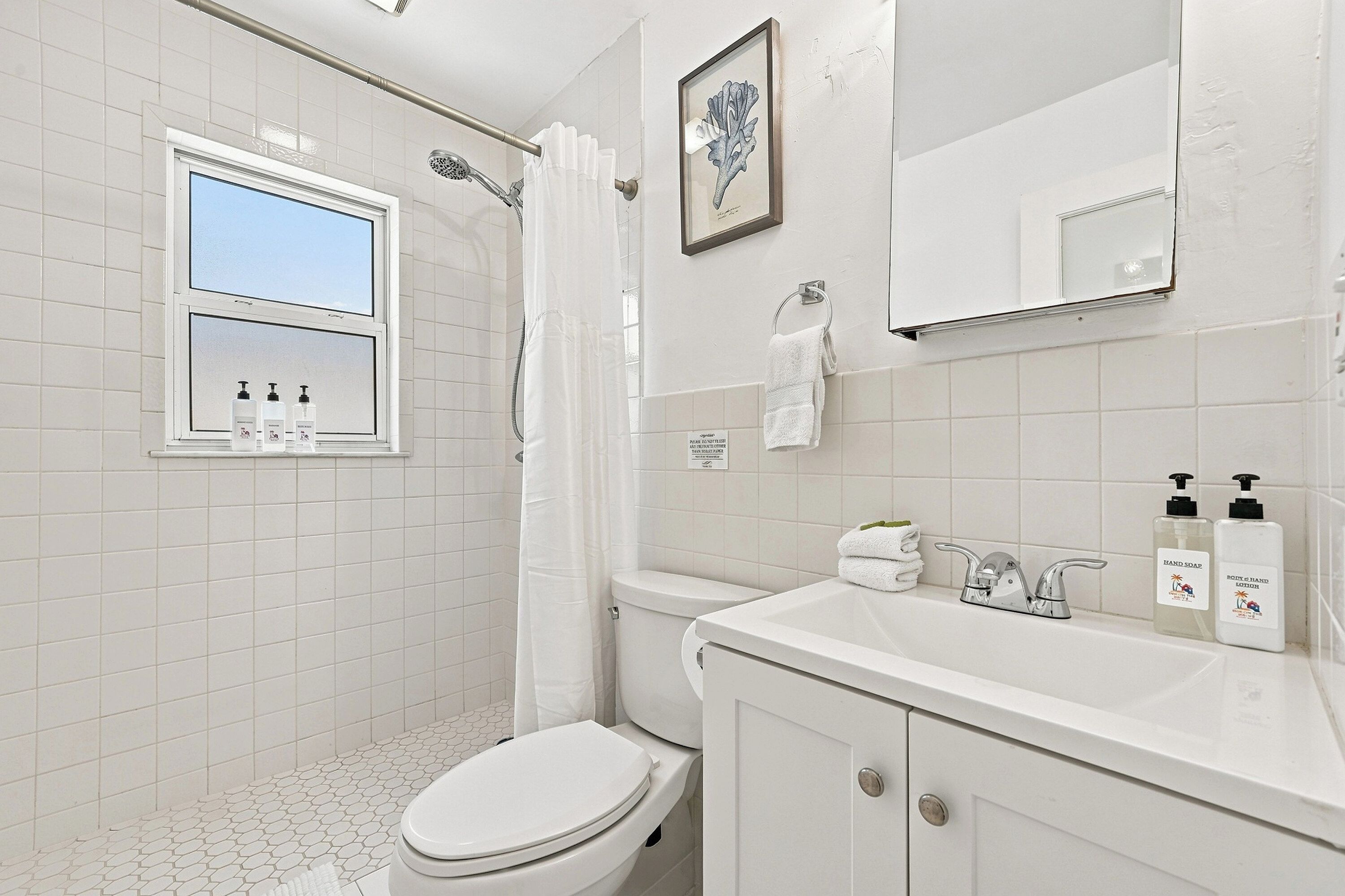 Un bagno moderno con il water, un lavandino e una doccia. Si vede una finestra sopra il water e un quadro appeso al muro.