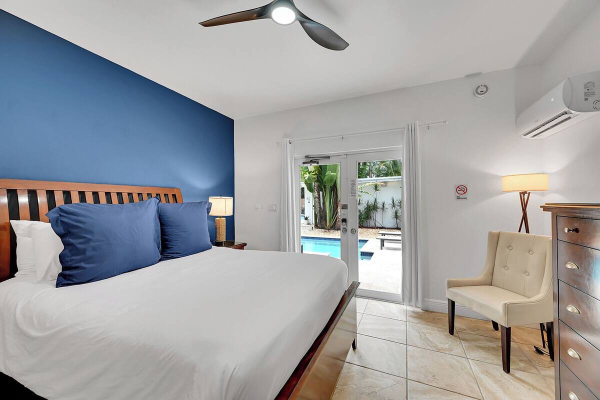 A hotel room with a bed, a chair, a desk, and a view of an outdoor pool.