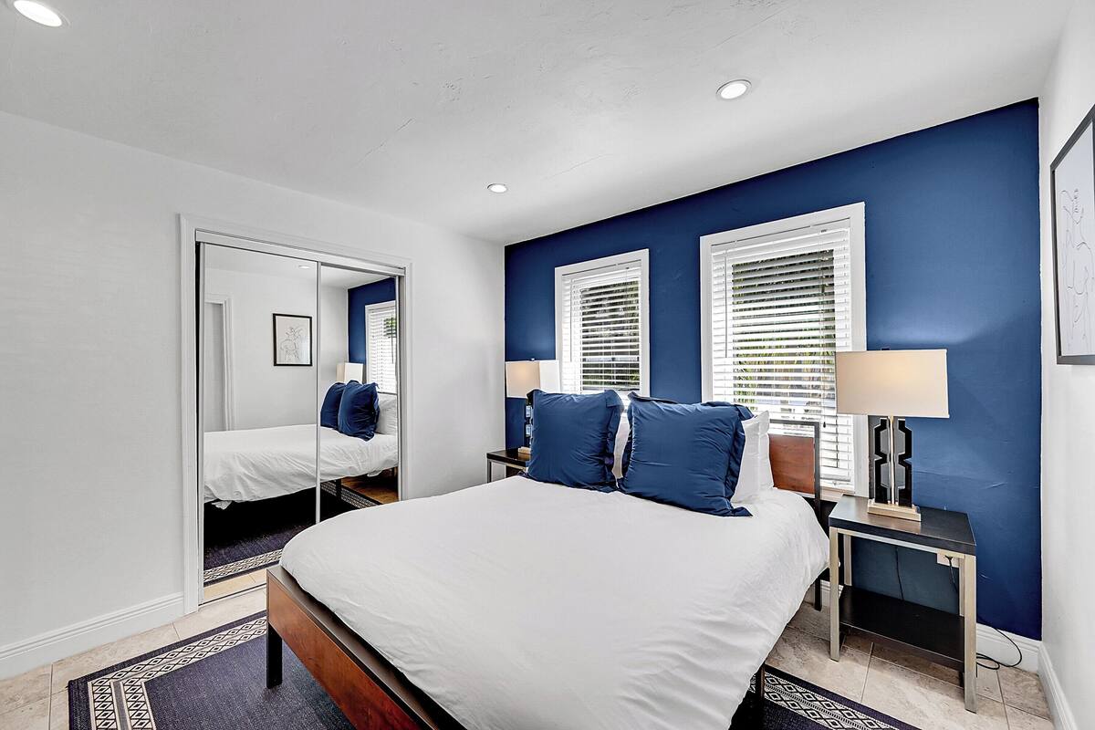A bedroom with a large bed, two bedside tables with lamps, a mirror, and a wardrobe.