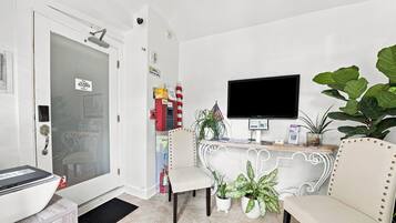 A modern living room with a flat-screen TV mounted on the wall, a white sofa, two chairs, a coffee table, and a potted plant.