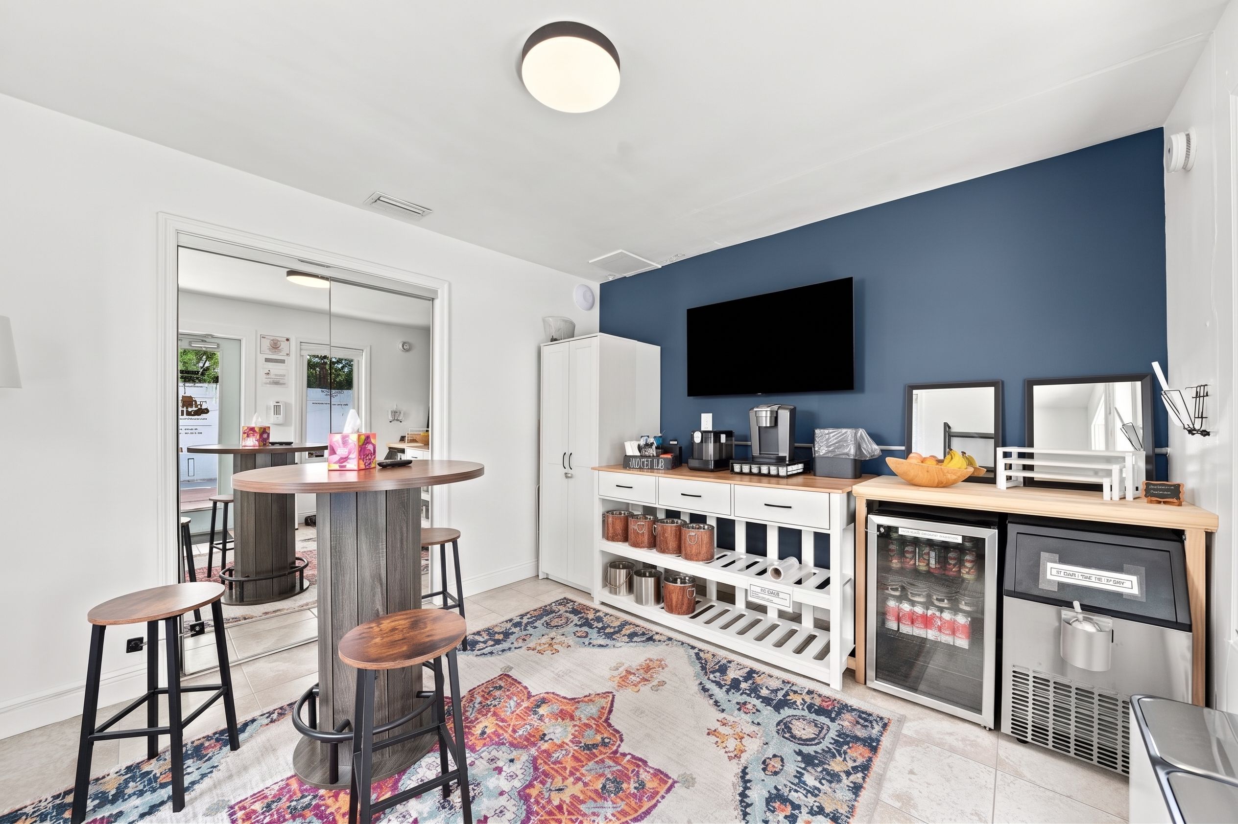 A modern kitchen with a round dining table, bar stools, a built-in fridge, and a TV mounted on the wall.
