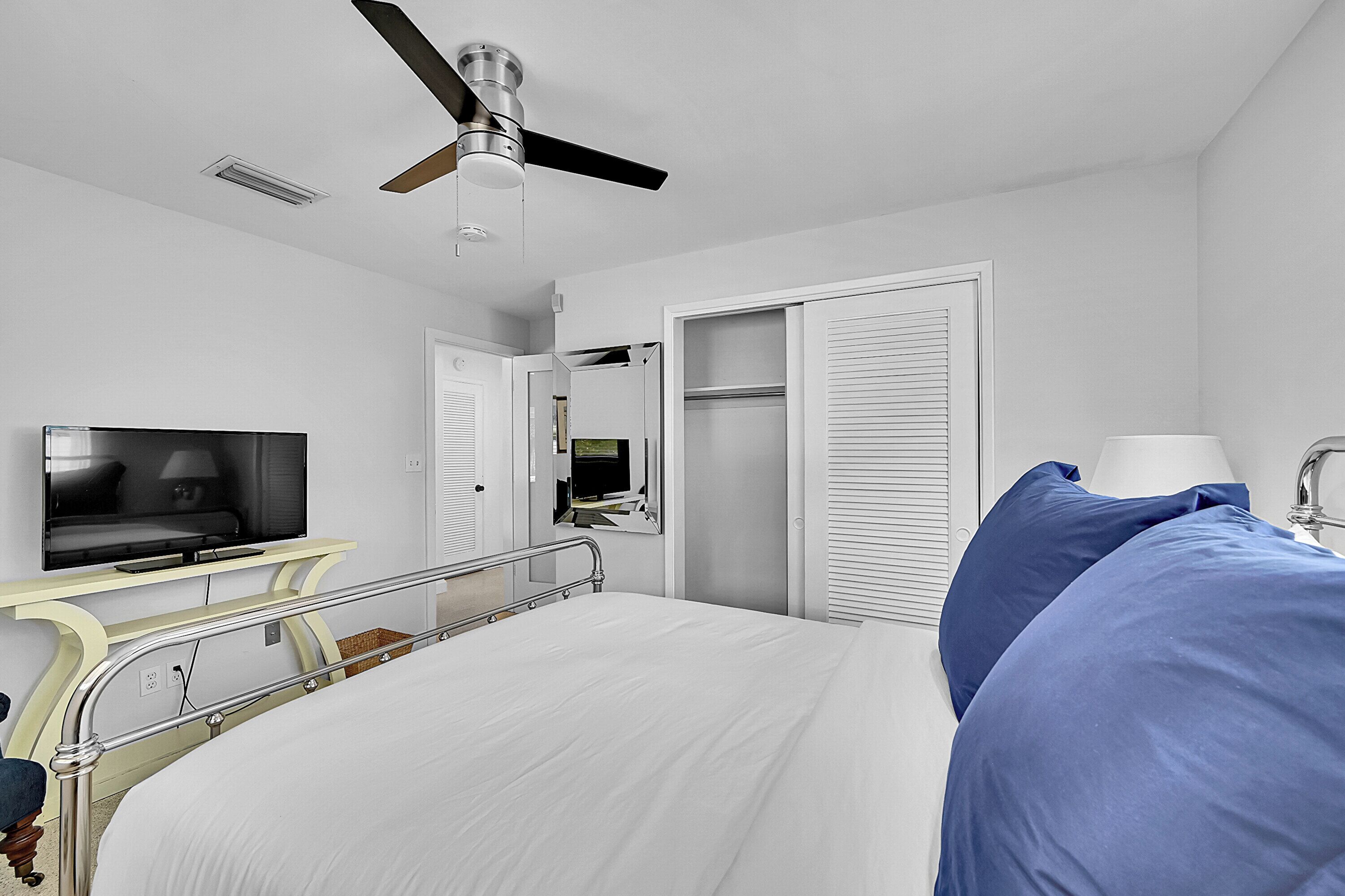 A hotel room with a bed, a television, a ceiling fan, and a wardrobe.