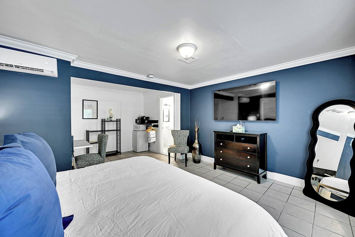 A bedroom with a large bed, a dresser, a chair, and a mirror.