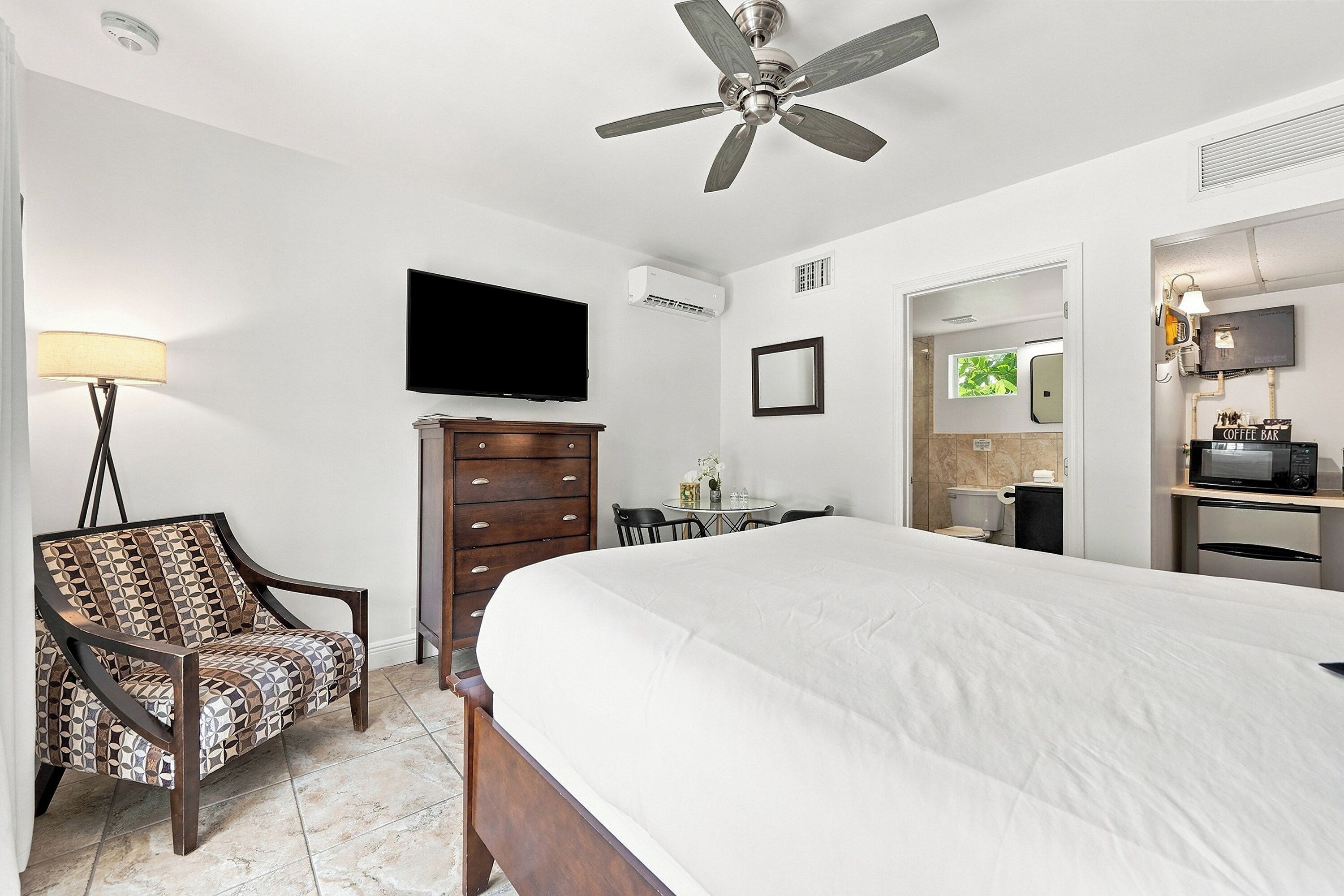 A hotel room with a bed, a chair, a dresser, a television, and a ceiling fan.