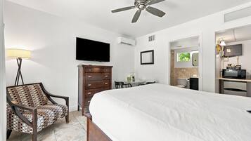 A hotel room with a bed, a chair, a dresser, a television, and a ceiling fan.
