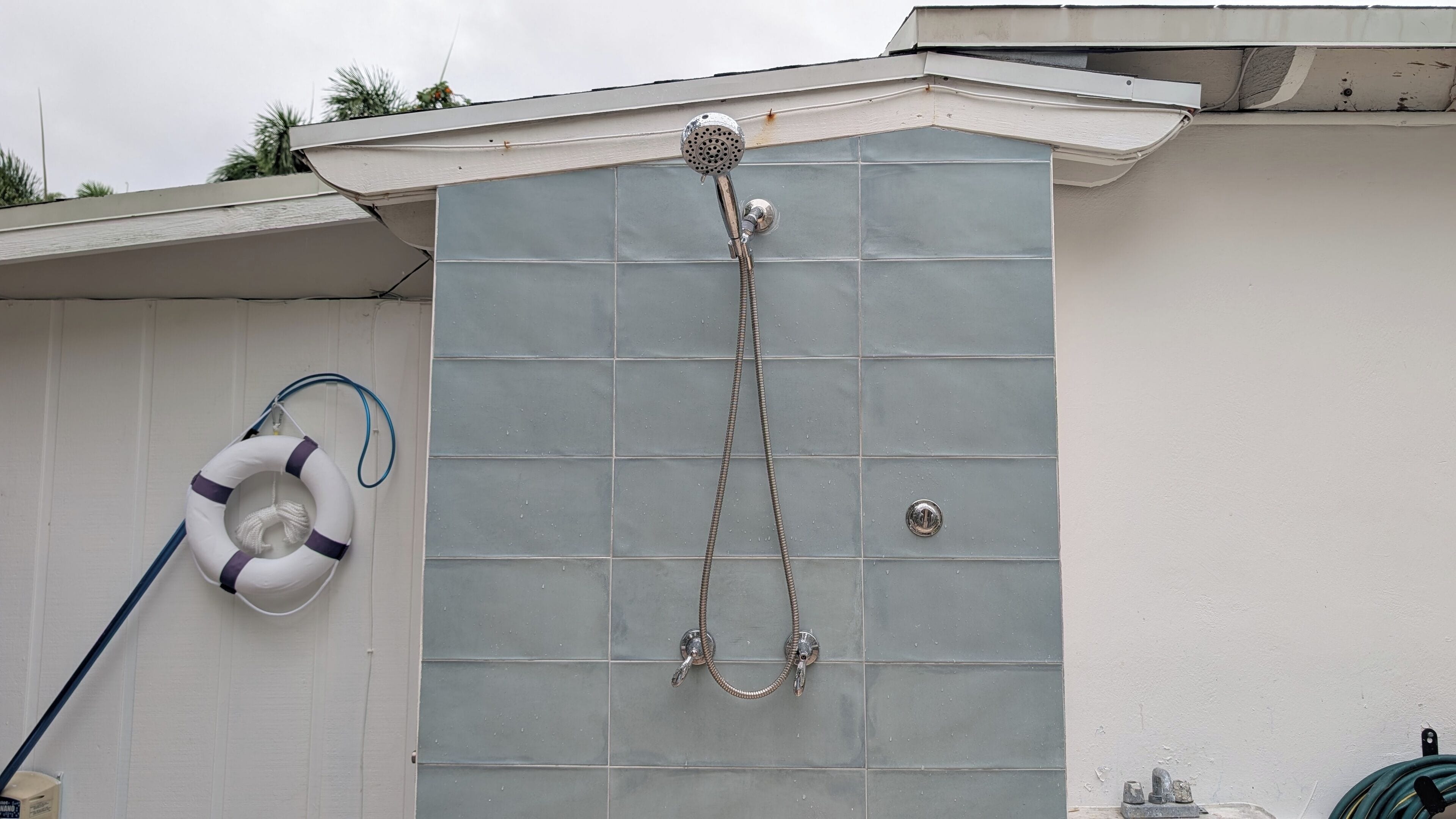 Un pommeau de douche fixé à un mur carrelé, avec un gilet de sauvetage accroché à proximité.