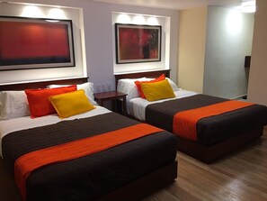 Habitación de hotel con dos camas, cada una con colcha negra y naranja, almohadas blancas y una mesita de noche de madera.
