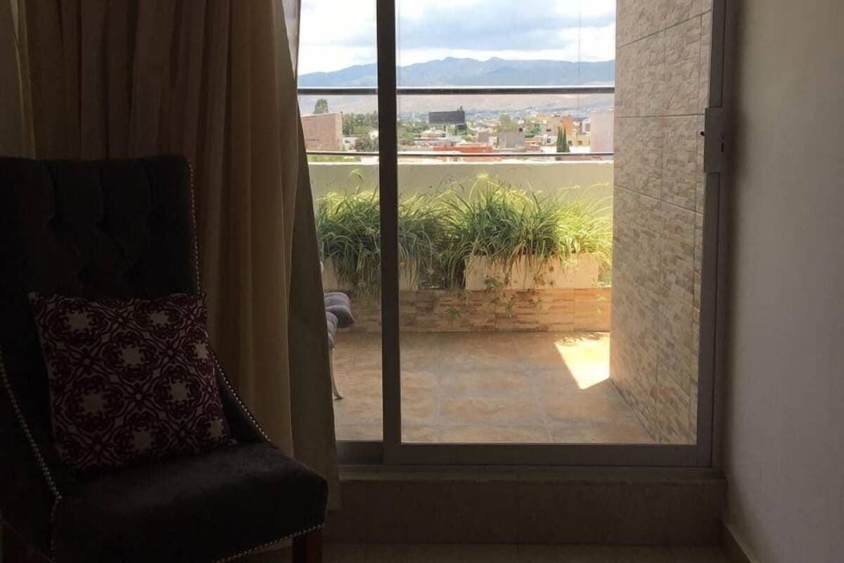 A room with a sliding glass door leading to a balcony, a chair with a patterned cushion, and a tiled floor.