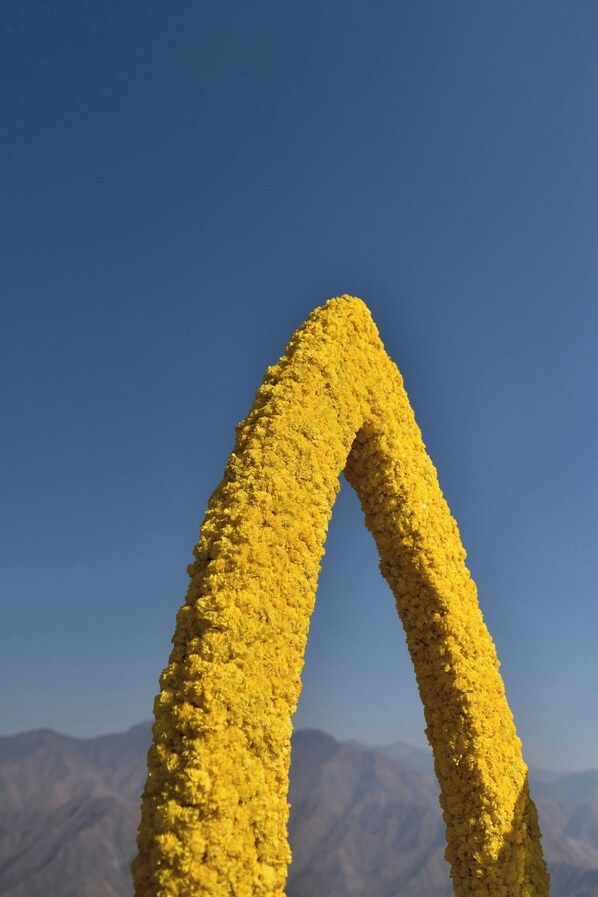 A yellow, textured arch structure against a clear blue sky.