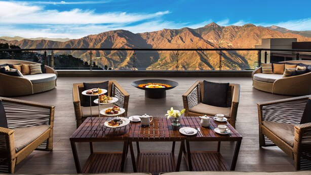 A rooftop terrace with wicker furniture, a dining table set with plates and a fire pit.