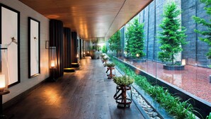A corridor with wooden flooring, framed artwork on the walls, and potted plants along the walkway.