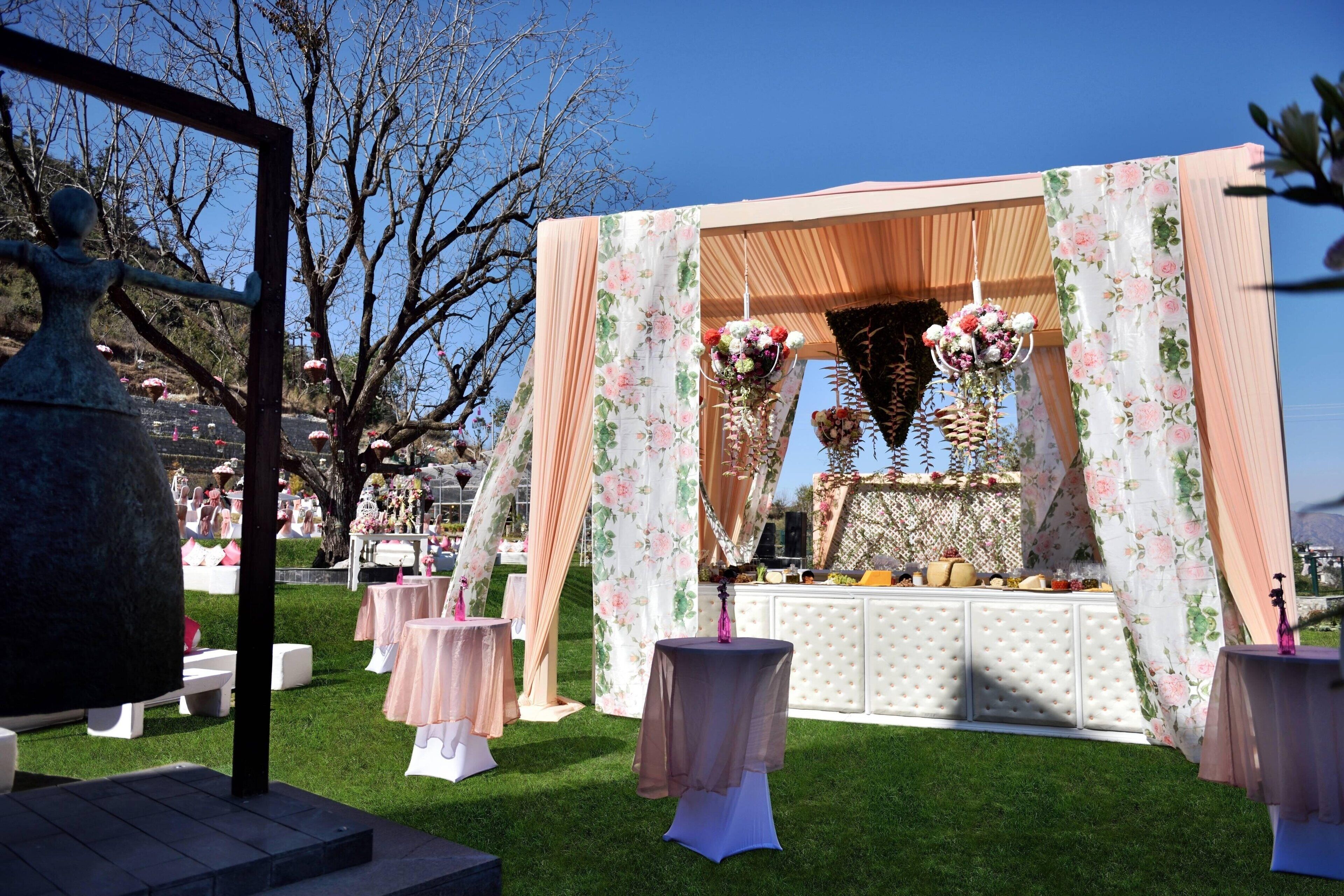 Montaje para un evento al aire libre con un fondo floral, mesas y una zona de bufé.