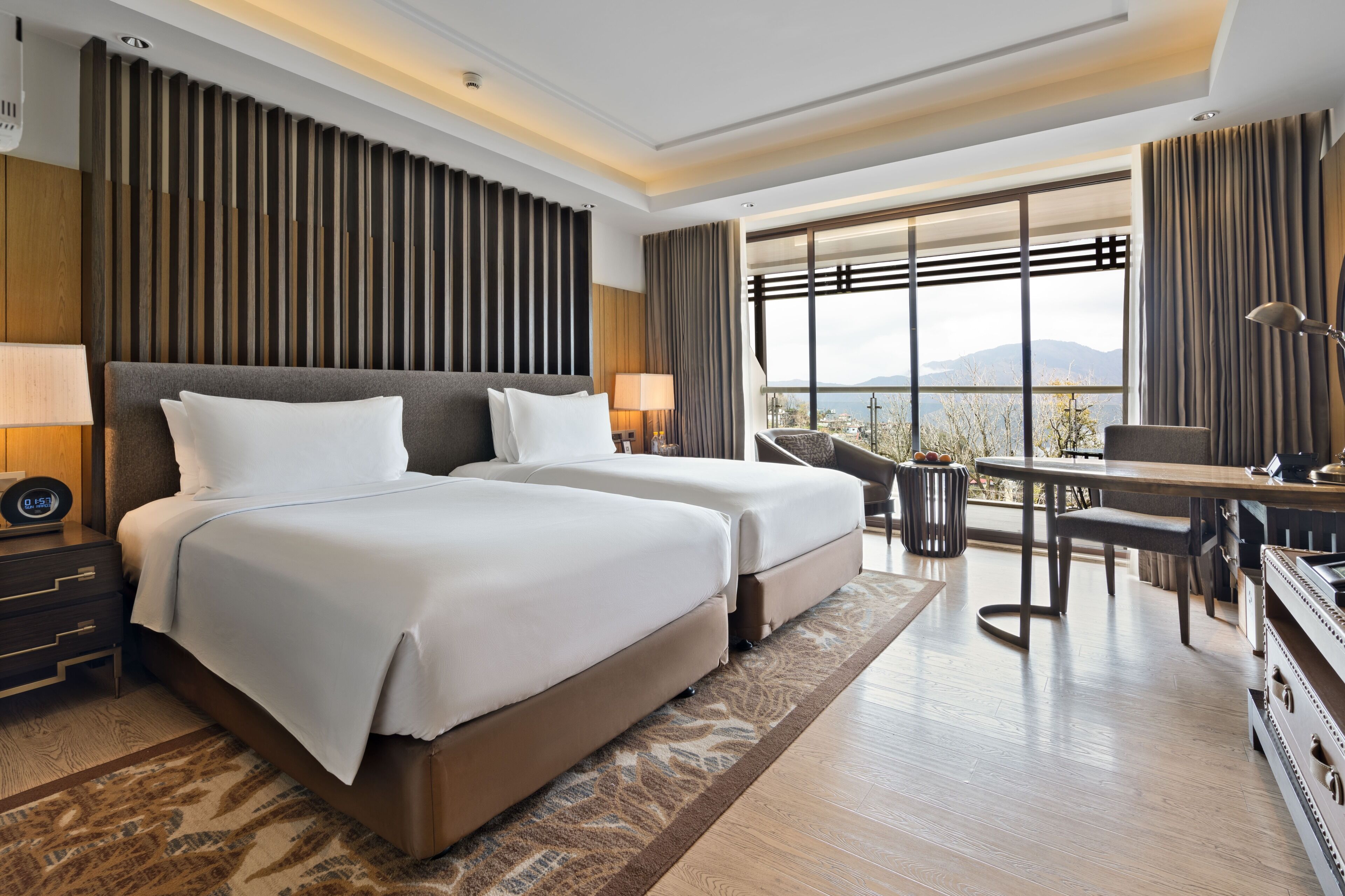 Quarto de hotel com duas camas, uma escrivaninha e vista para as montanhas.