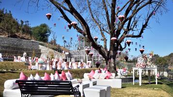 An outdoor event with a stage, white seating, and a tree with hanging decorations.