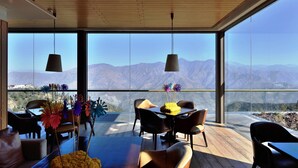 A modern dining area with a table set for two, large windows offering a mountain view, and hanging pendant lights.