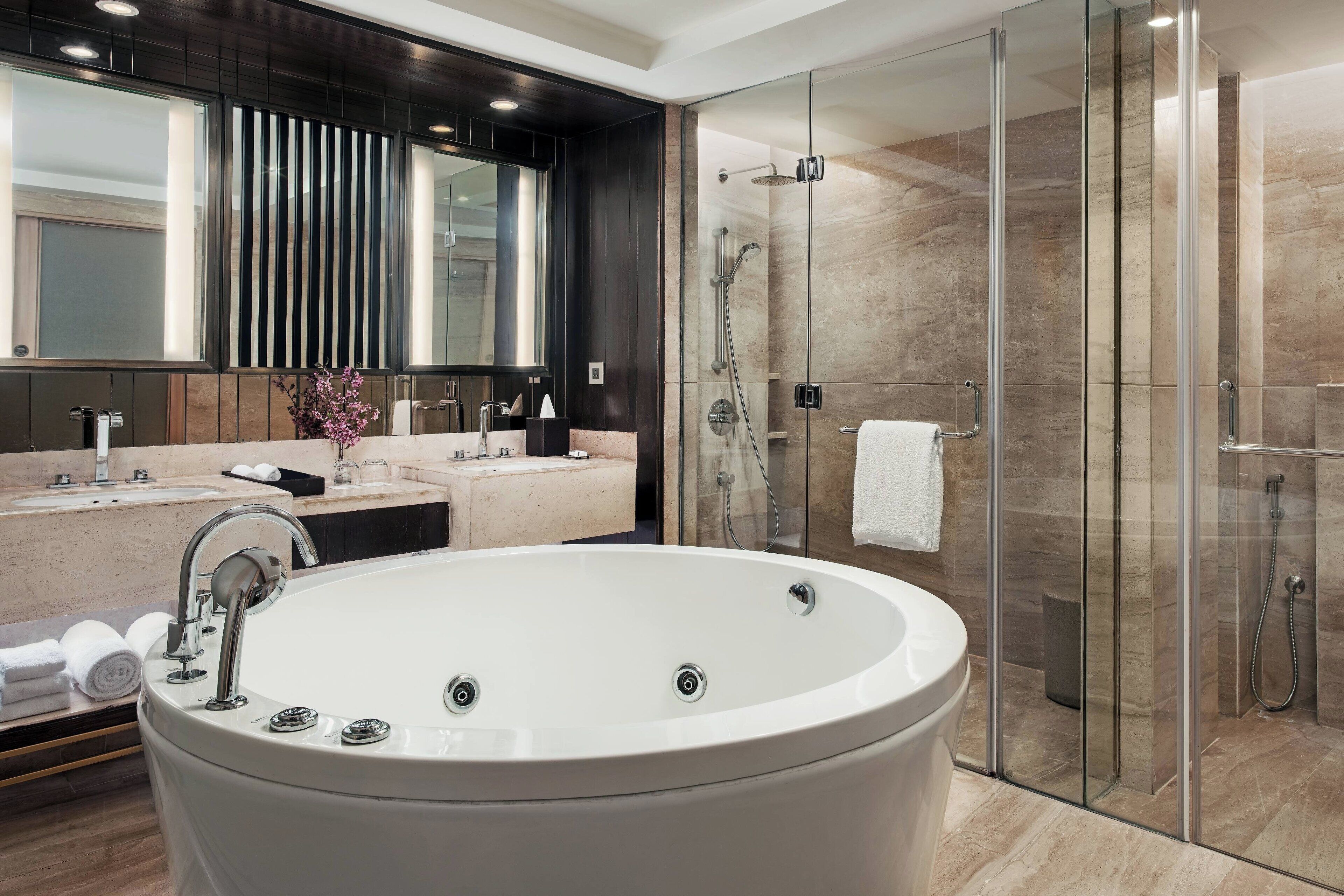 Un baño moderno con una bañera grande, una ducha con mampara de vidrio y un tocador con espejo y lavabo.
